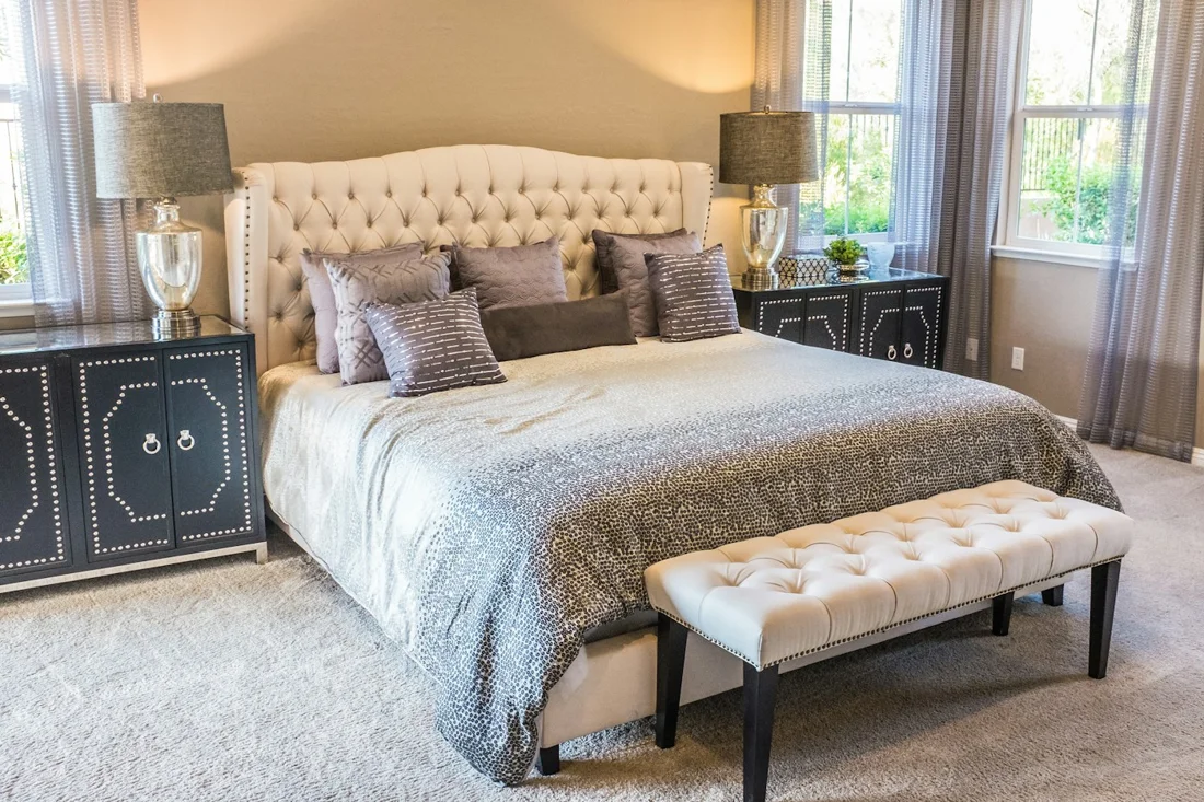 Bed with a cream tufted headboard, layered bedding and bedside cabinets