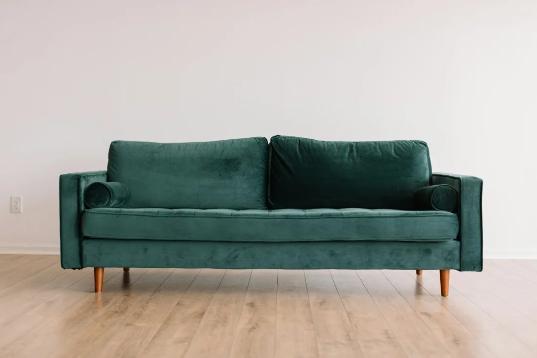 Green upholstered sofa with round cushions against a pale wall